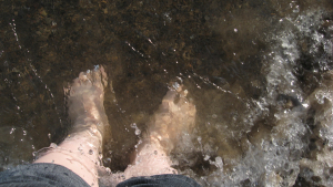 Water washes over two feet standing on a sandy beach